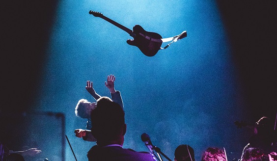 En gitarrist kastar en gitarr i luften på scenen