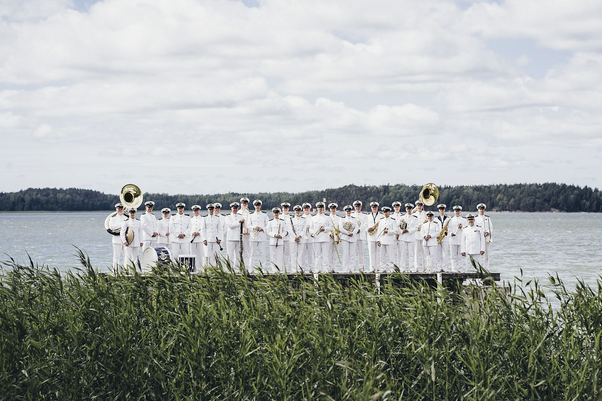 Laivaston soittokunta seisoo muodossa järven rannalla valkoisissa puvuissa 